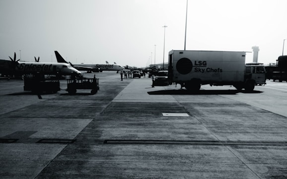 An airport tarmac with several parked aircraft from SpiceJet and a catering truck labeled 'LSG Sky Chefs'. The scene is busy with airport personnel and various ground service equipment visible. The image appears to be taken on a clear day with a control tower in the background.