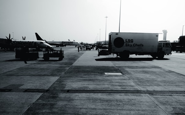 An airport tarmac with several parked aircraft from SpiceJet and a catering truck labeled 'LSG Sky Chefs'. The scene is busy with airport personnel and various ground service equipment visible. The image appears to be taken on a clear day with a control tower in the background.