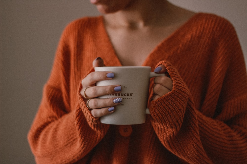 Femme en pull rouge tenant une tasse en céramique blanche