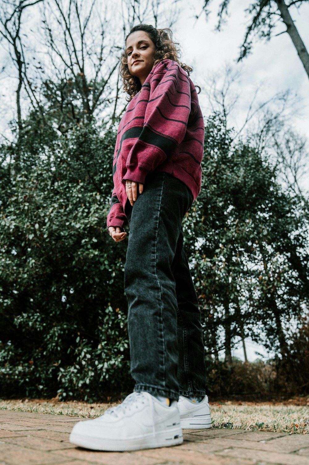 man in red and black jacket and blue denim jeans standing near green trees during daytime