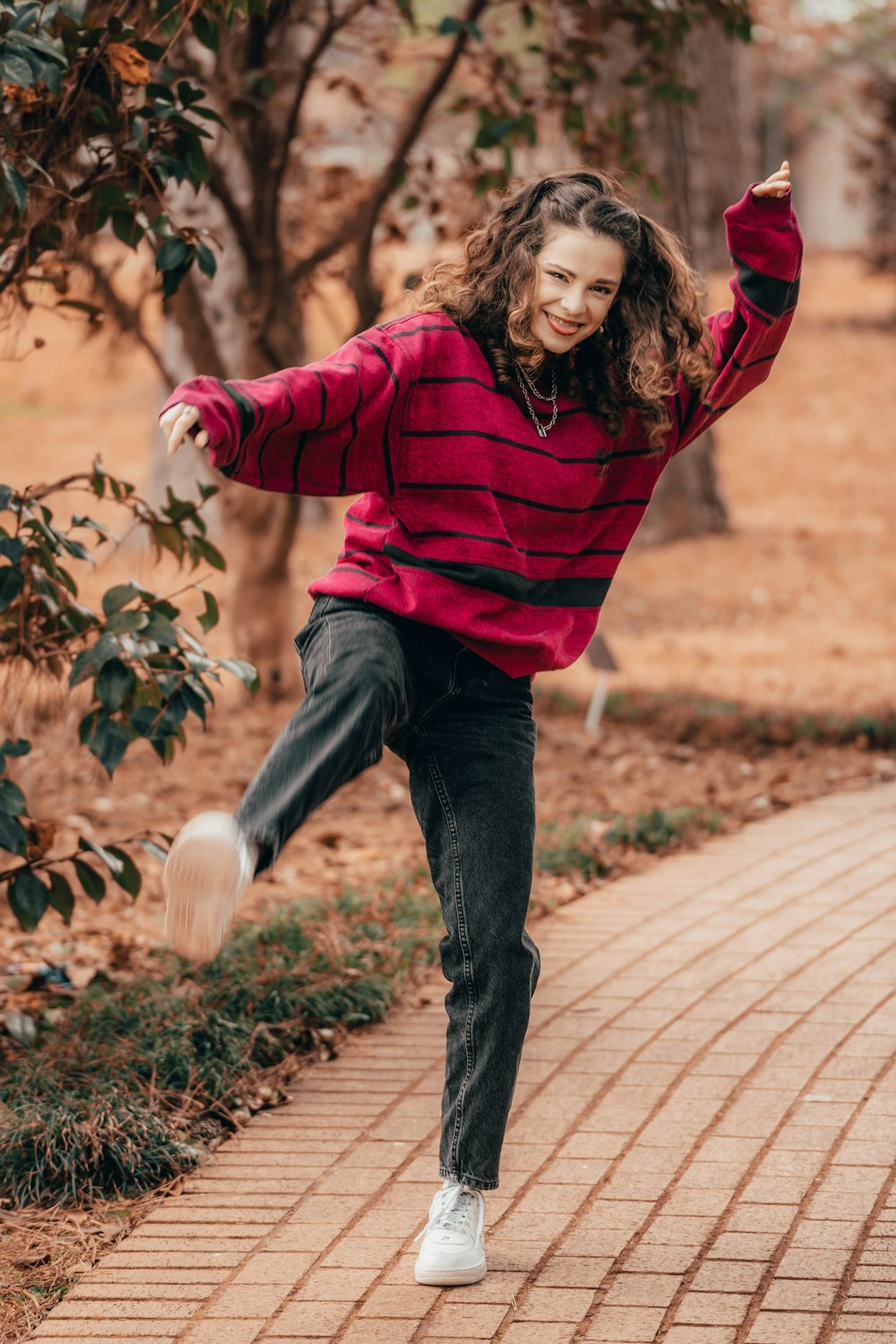 woman in red long sleeve shirt and blue denim jeans jumping on brown brick pathway during