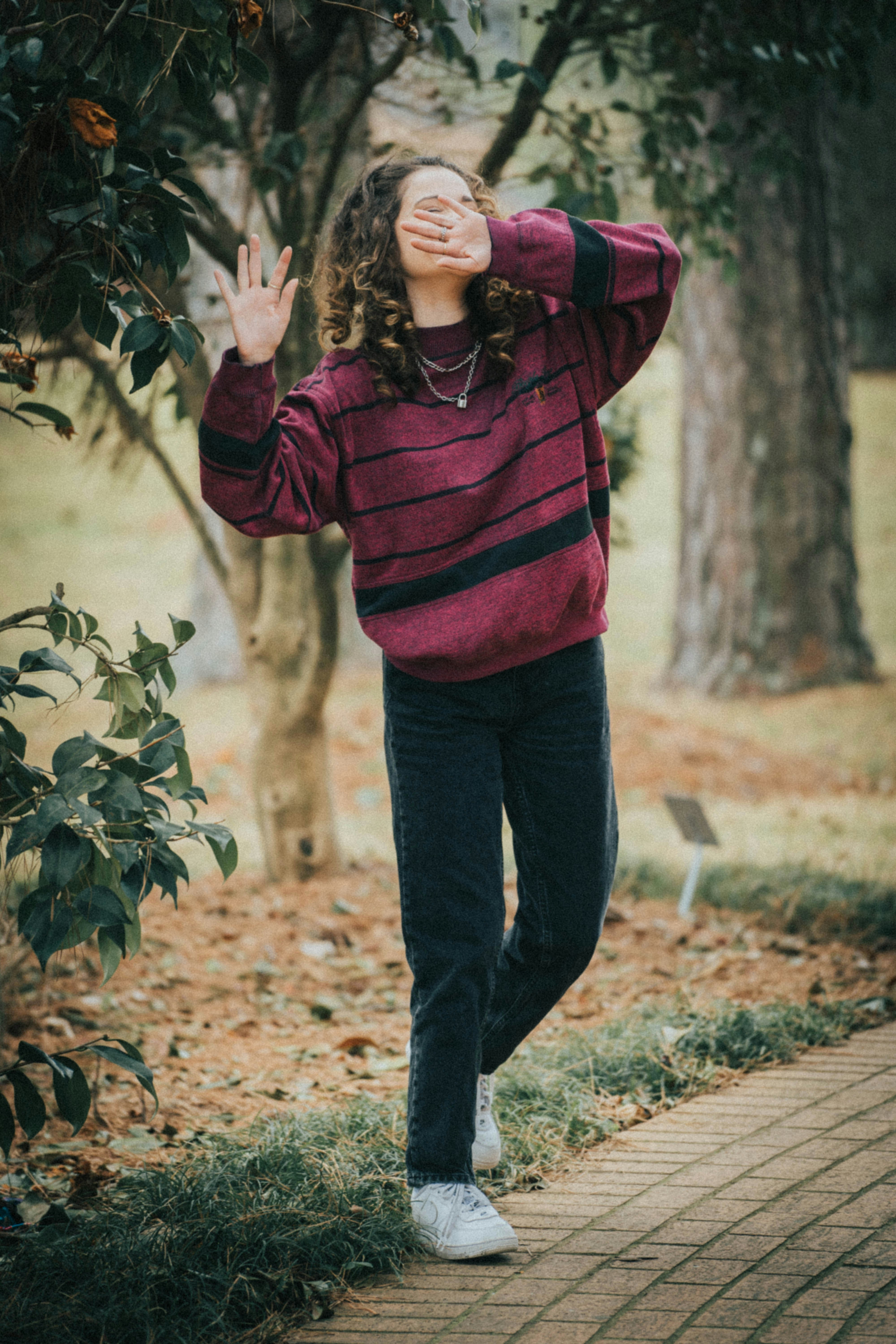 woman in red and black striped hoodie standing on brown dried leaves during daytime