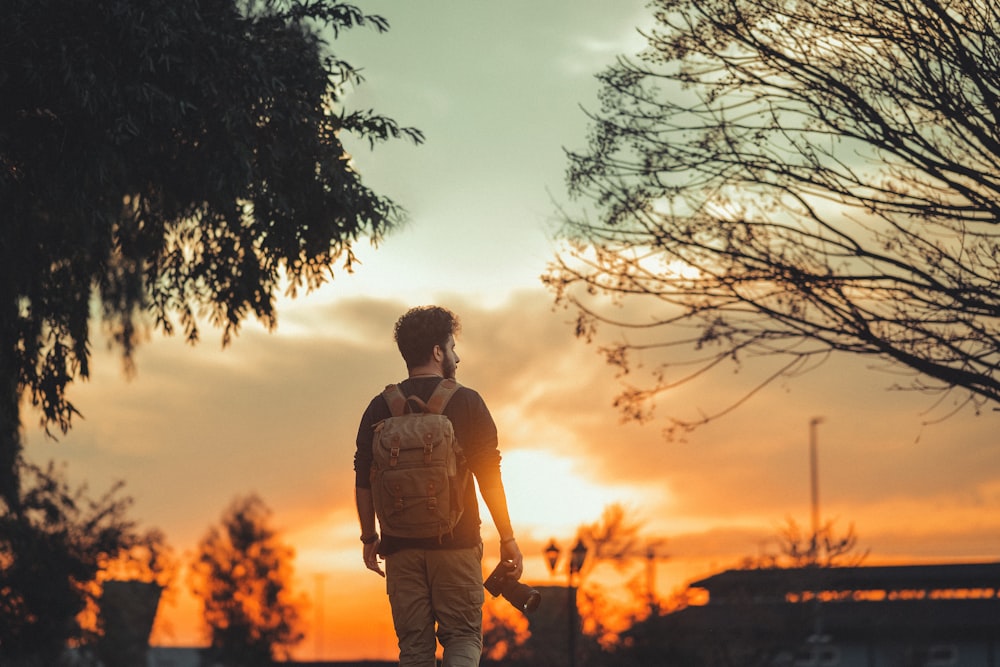 man in brown shirt standing beside tree during sunset