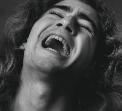A close-up black and white photograph of a person experiencing a strong emotion, likely during an intense moment or expression of agony. The person's mouth is open wide, eyes are partially closed, and the features are dramatically lit, highlighting the texture of the skin and hair.