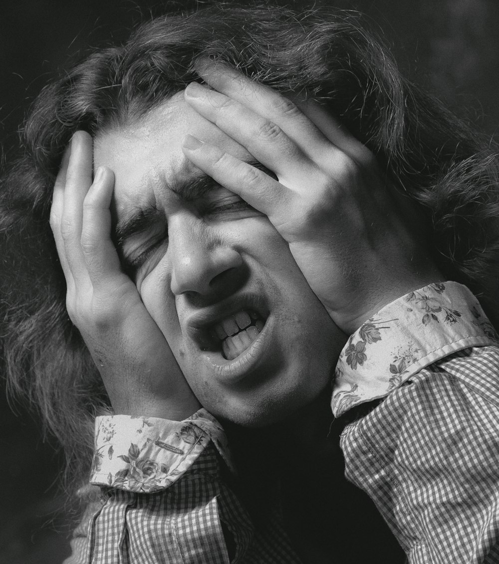 woman in white and black checkered dress shirt covering her face with her hand