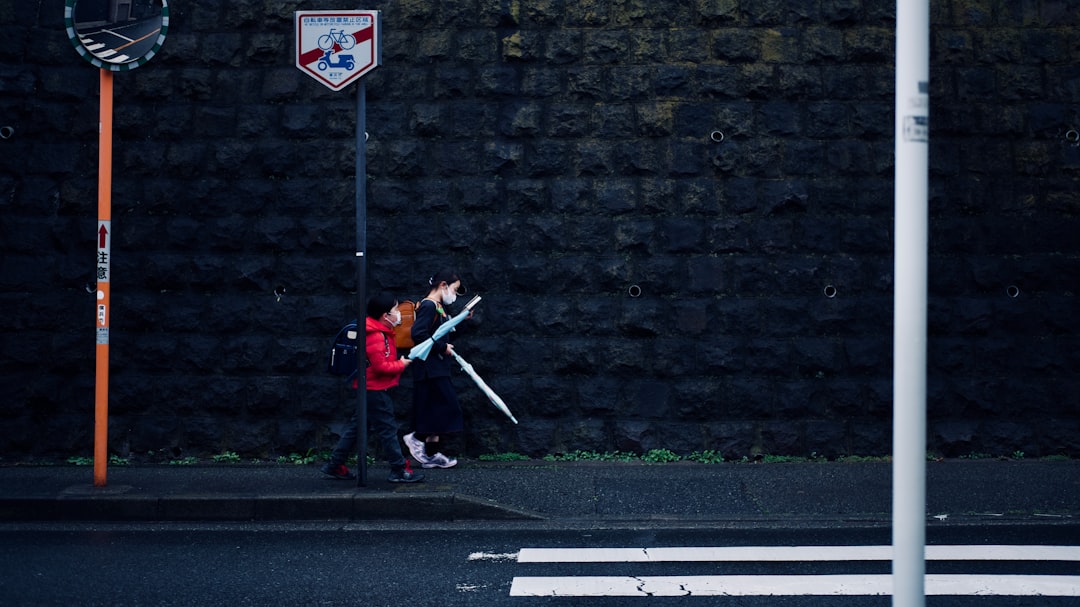 man in red jacket and black pants walking on sidewalk during daytime