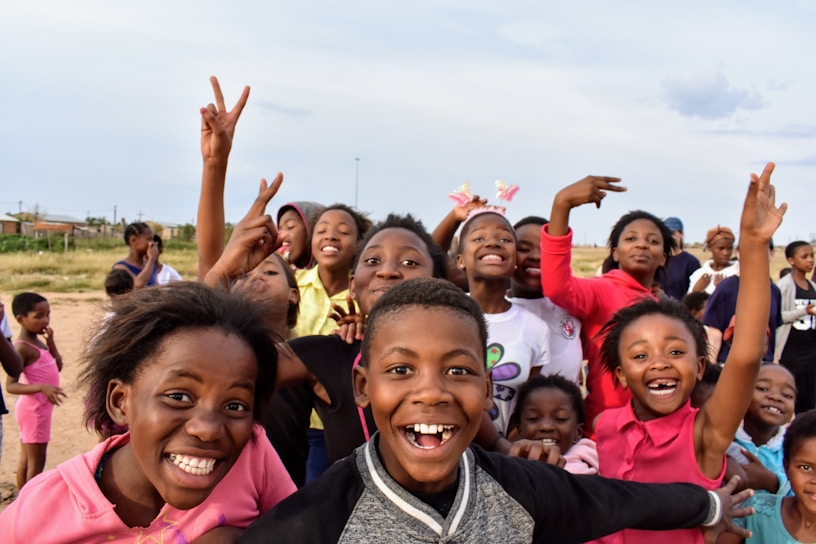 A group of joyful Ugandan children playing together under a bright blue sky.