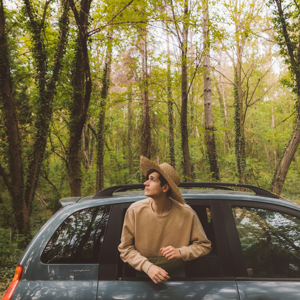 Un gars portant un chapeau regardant à travers une fenêtre en regardant un beau monde naturel vert autour de lui