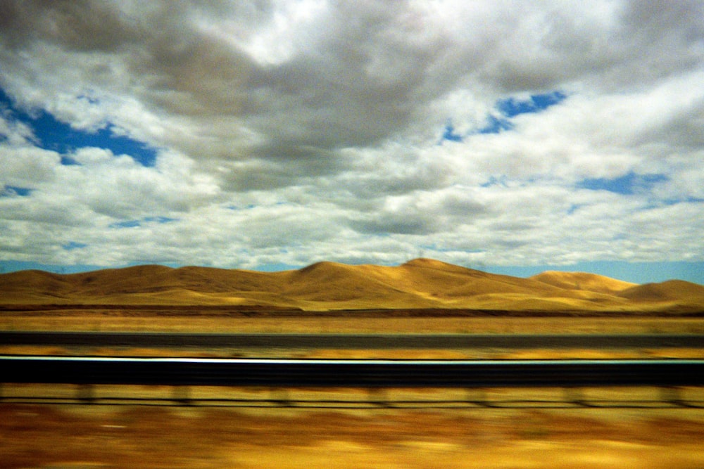 brown mountains near body of water under white clouds during daytime