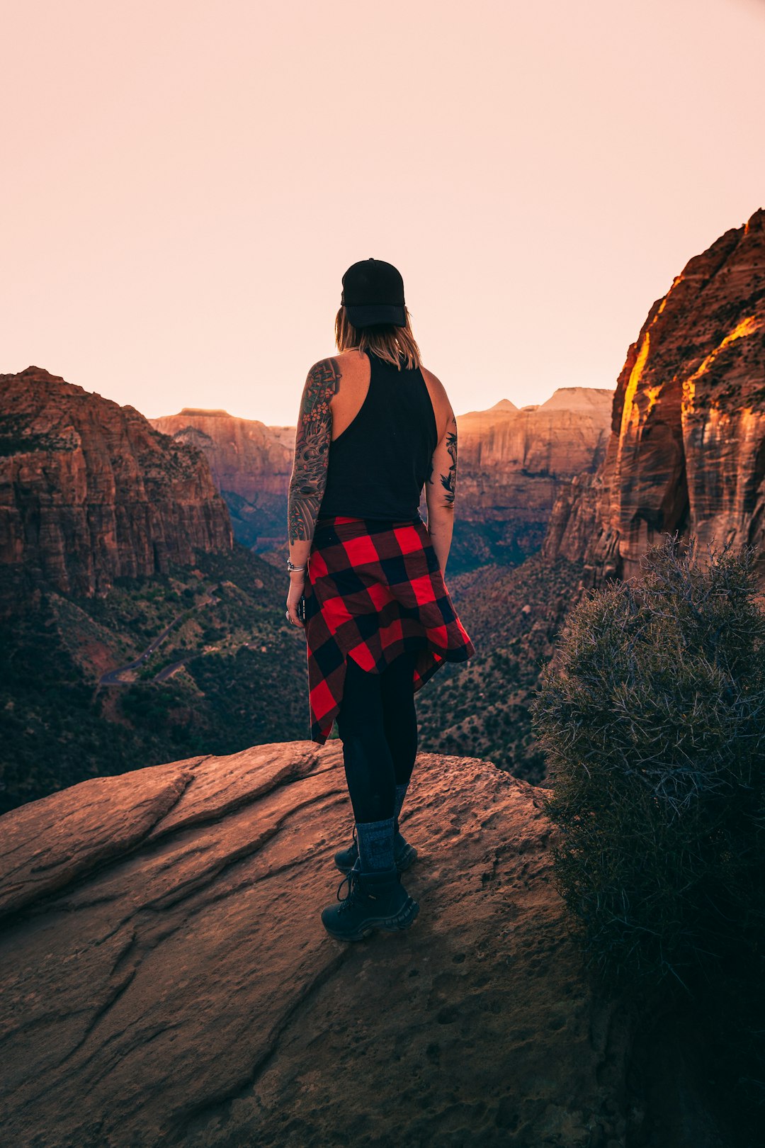 woman in black tank top and red and black plaid skirt standing on brown rock formation