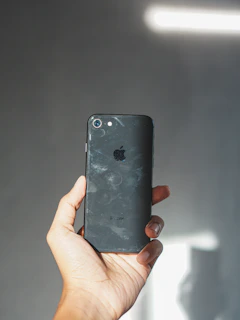 Hands holding a gently used smartphone with a clean, scratch-free screen against a soft background.