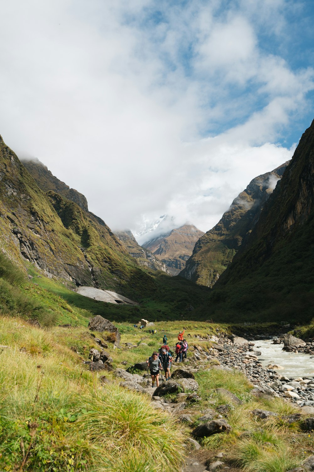 people walking on green grass field near mountains under white clouds during daytime