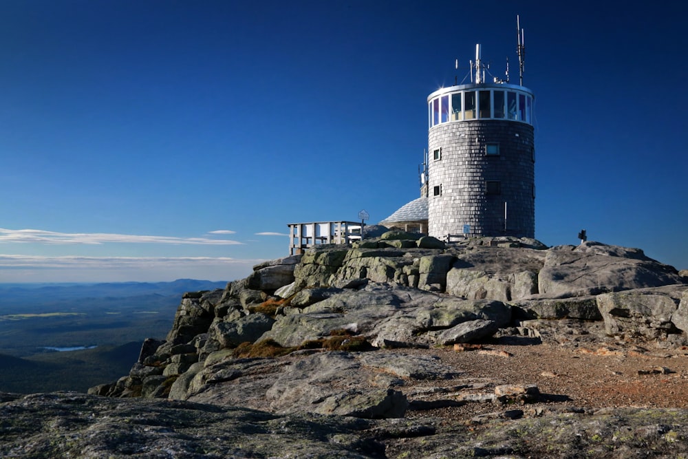 farol branco e preto na colina rochosa perto do corpo de água durante o dia