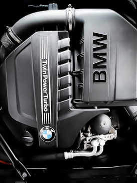 A close-up image of a BMW engine featuring the TwinPower Turbo logo prominently displayed. The engine components are clean and well-defined, showcasing modern automotive engineering.