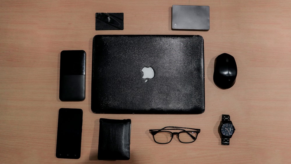 silver macbook beside black framed eyeglasses on brown wooden table