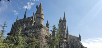 A bright Minecraft scene showing a tall castle with flag towers and hidden caves nearby, under a clear blue sky.