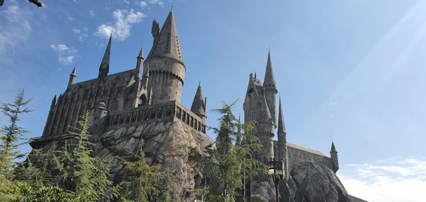 A bright Minecraft scene showing a tall castle with flag towers and hidden caves nearby, under a clear blue sky.