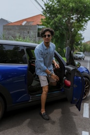 man in blue blazer leaning on blue car