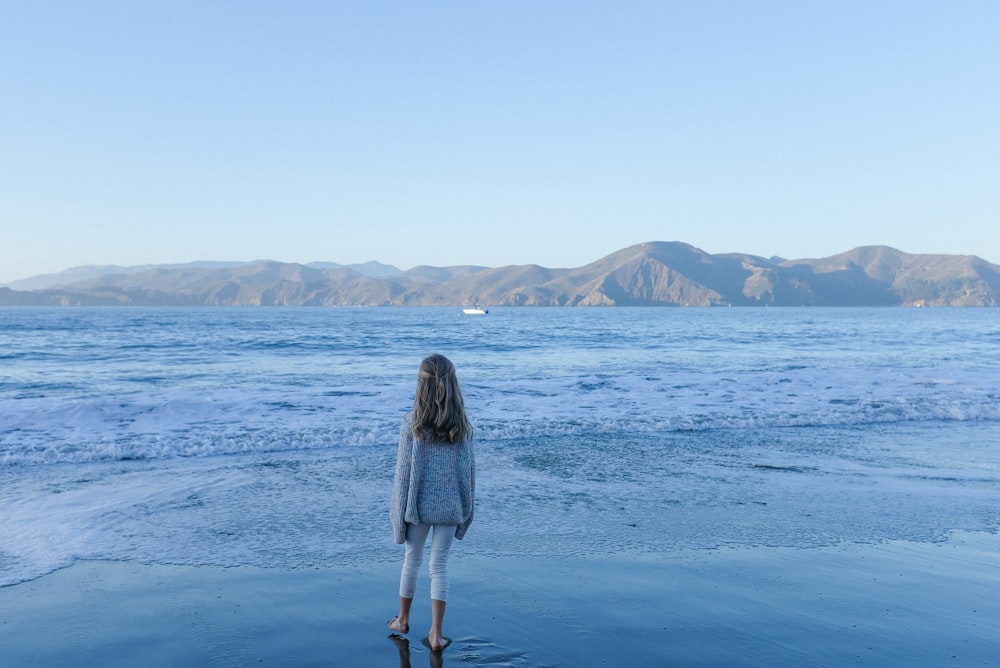 woman in white and black long sleeve dress standing on seashore during daytime