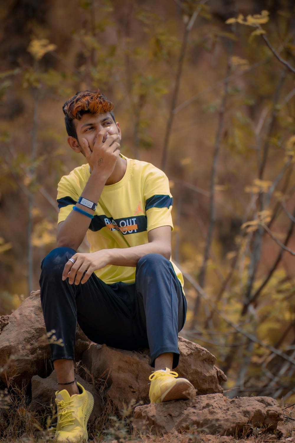man in yellow polo shirt and blue pants sitting on brown rock during daytime
