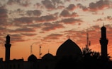 Sunset silhouette of mosque domes with people walking nearby