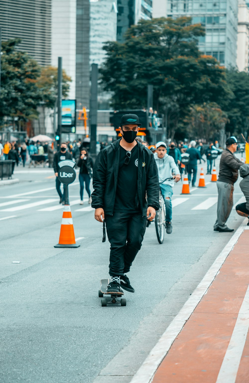 man in black jacket and black cap riding on black kick scooter on gray concrete road