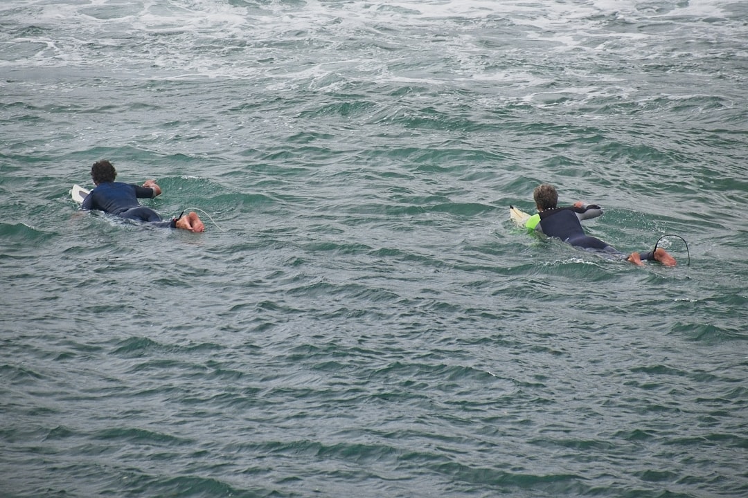 2 people in blue and black wet suit on body of water during daytime