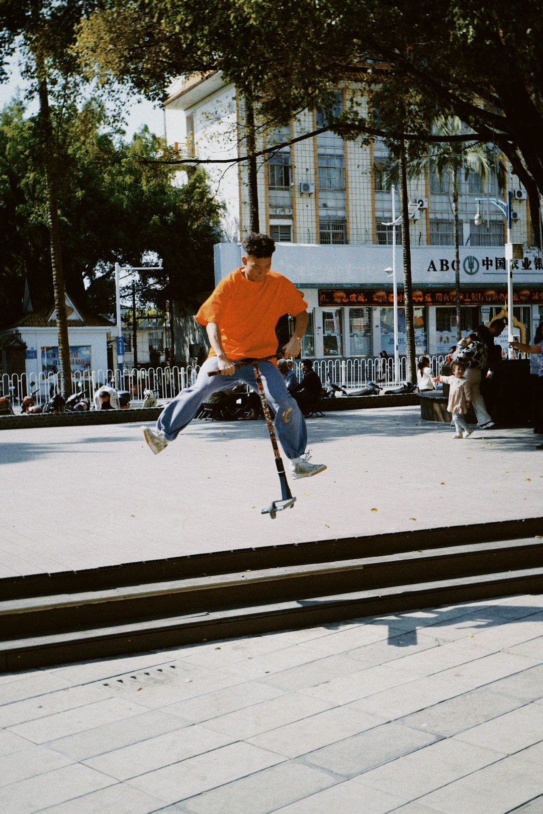 man in orange shirt and blue denim jeans riding on black skateboard during daytime