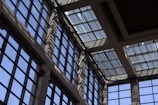 Sunlight streams through a series of large, grid-patterned glass windows, casting intricate shadow patterns on the interior walls. The design gives a modern and geometric aesthetic, with a mix of light and shadow creating a dynamic visual effect.