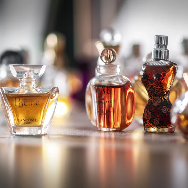 A clear glass perfume bottle in sharp focus catching warm sunlight against a blurred background