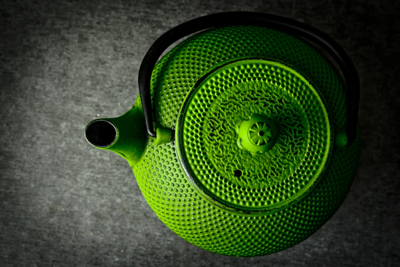 Close-up of a beautifully handcrafted Moroccan teapot with intricate golden patterns on a dark green background.