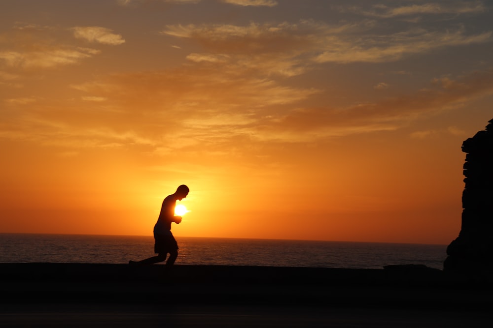 silhouette of man running on beach during sunset