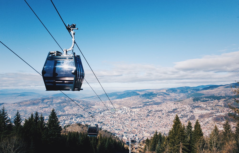 Teleférico negro sobre árboles verdes y montañas durante el día