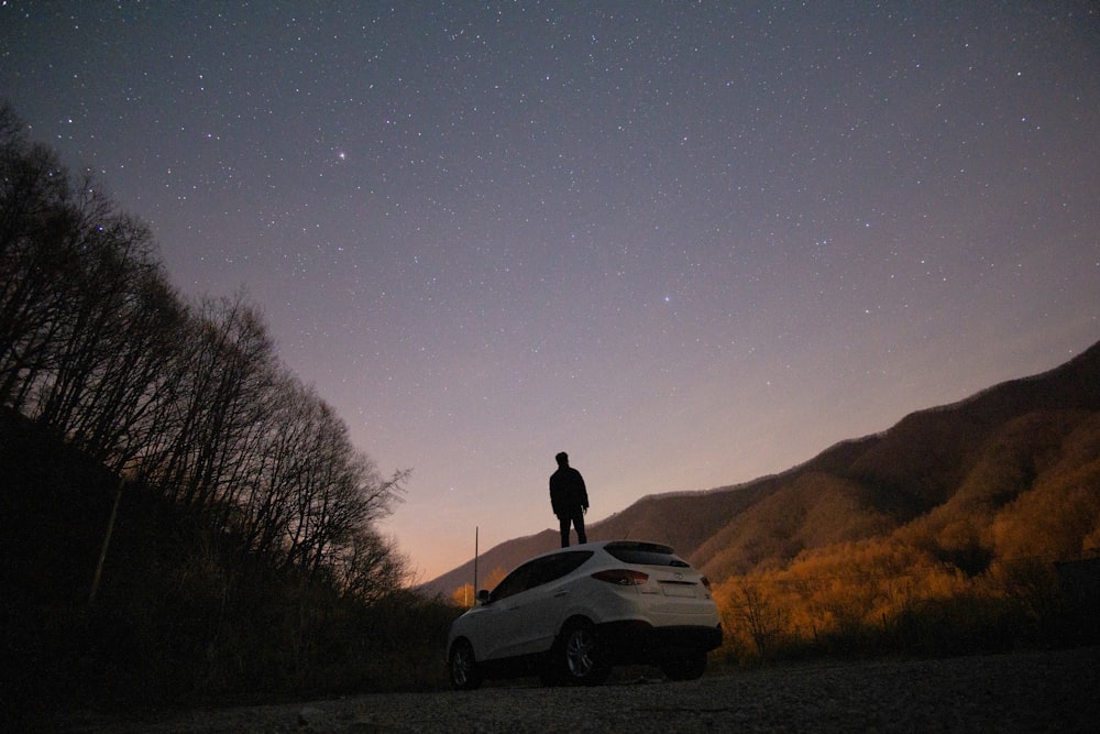 silhouette of man sitting on white car during night time