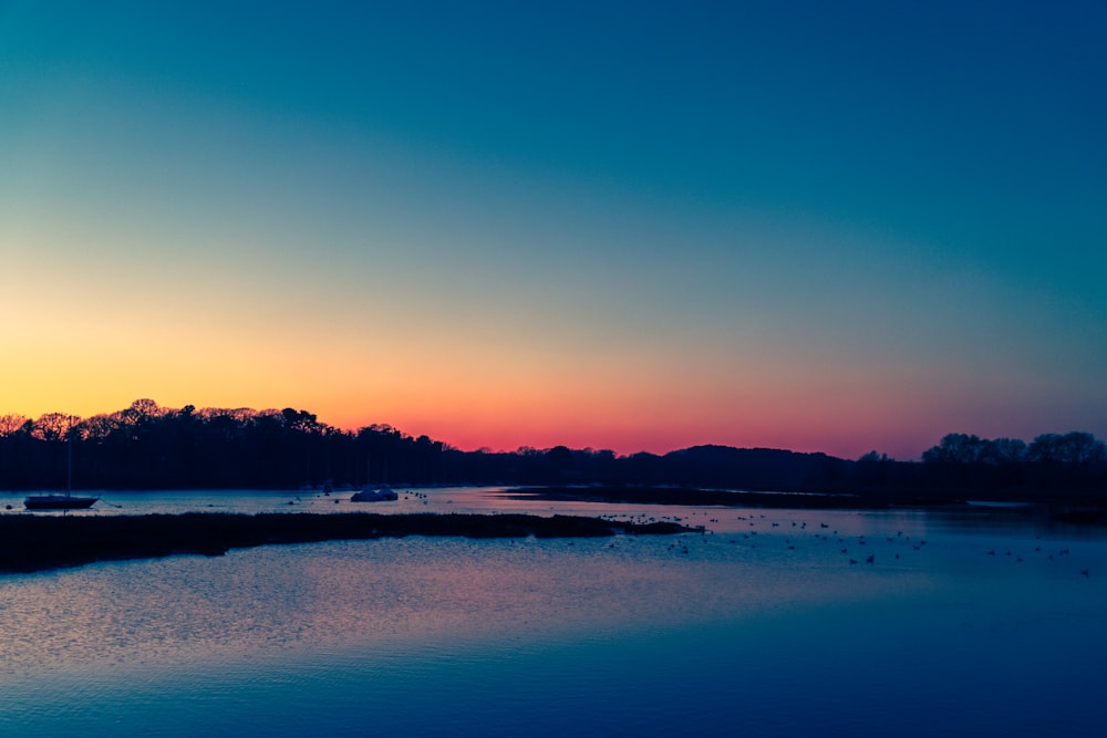 body of water near trees during sunset