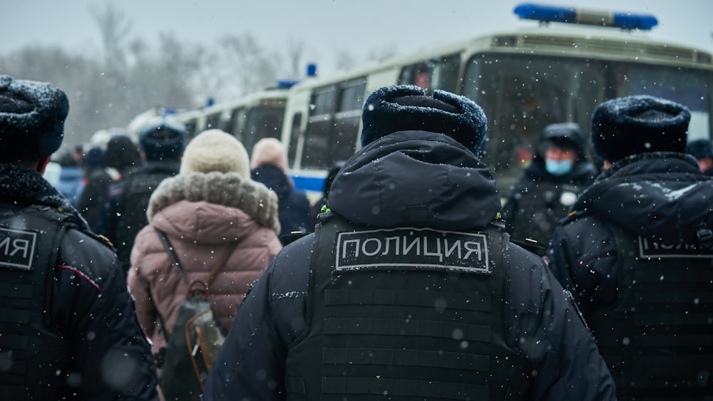 people in winter jackets standing near white car during daytime