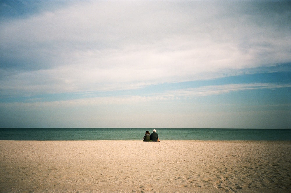 2 people sitting on beach sand during daytime