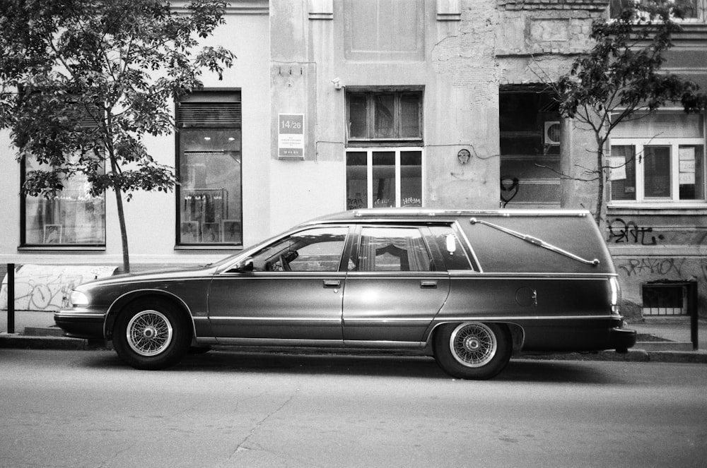 grayscale photo of sedan parked beside building