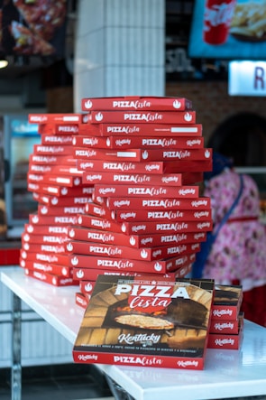 Stack of white pizza boxes with colorful logos neatly arranged on a rustic wooden table.