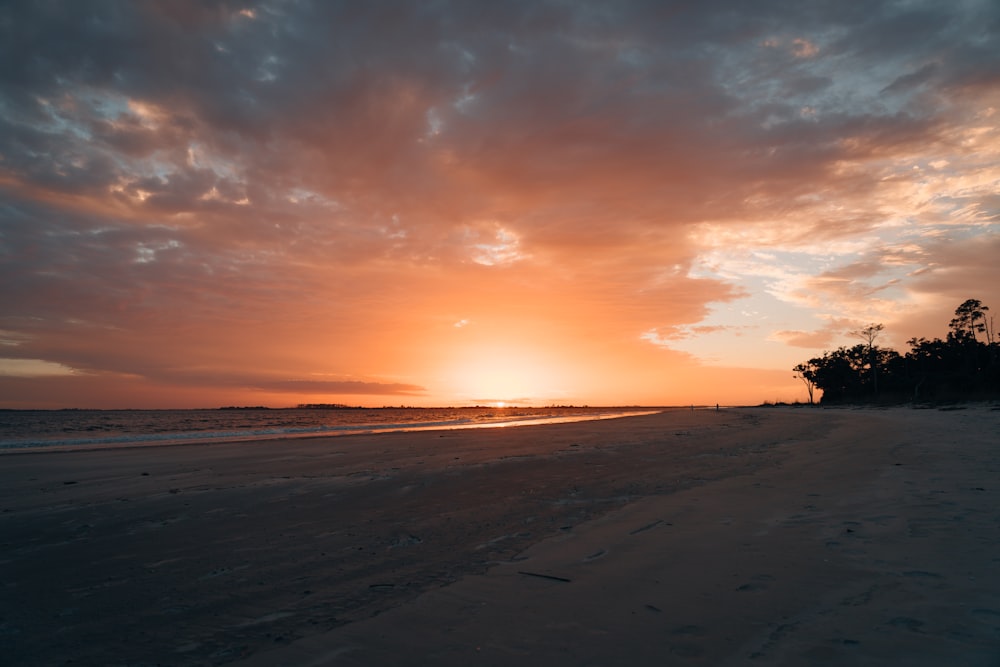 the sun is setting on the beach with the ocean in the background