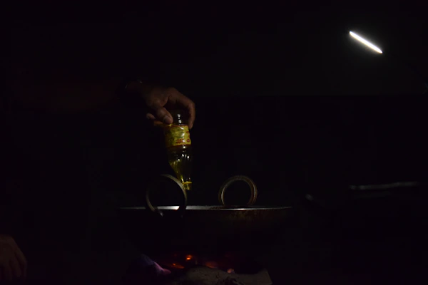 A hand pouring rich mustard oil into a traditional cooking pan, capturing the warm golden hue.