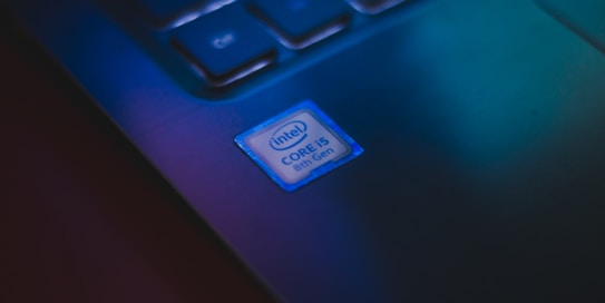 A close-up of a laptop keyboard focusing on a sticker that identifies an Intel Core i5 8th Gen processor. The lighting casts a bluish-green hue over the keyboard, creating a modern and tech-savvy atmosphere.