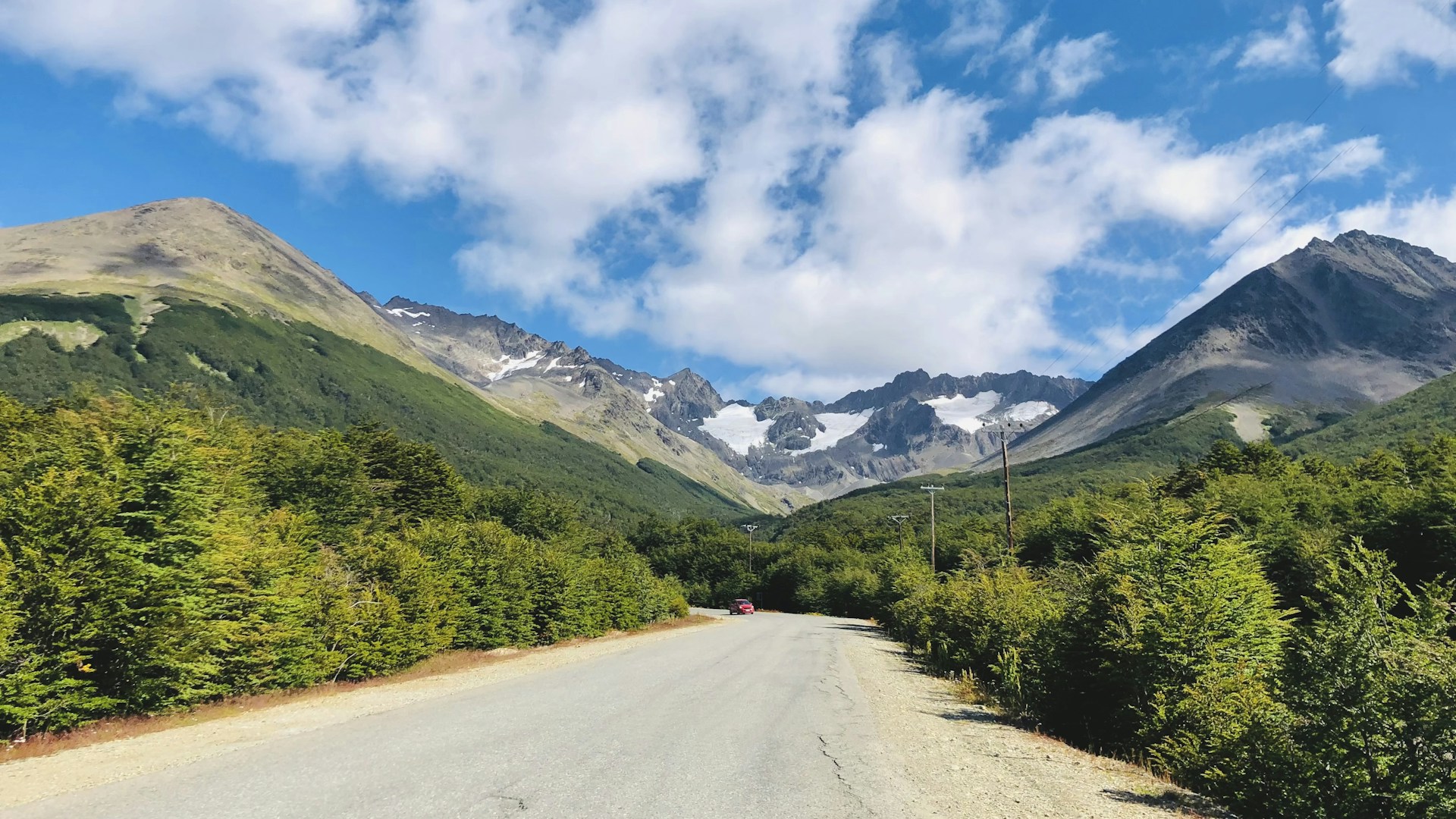 red car on road near green trees and mountains during daytime