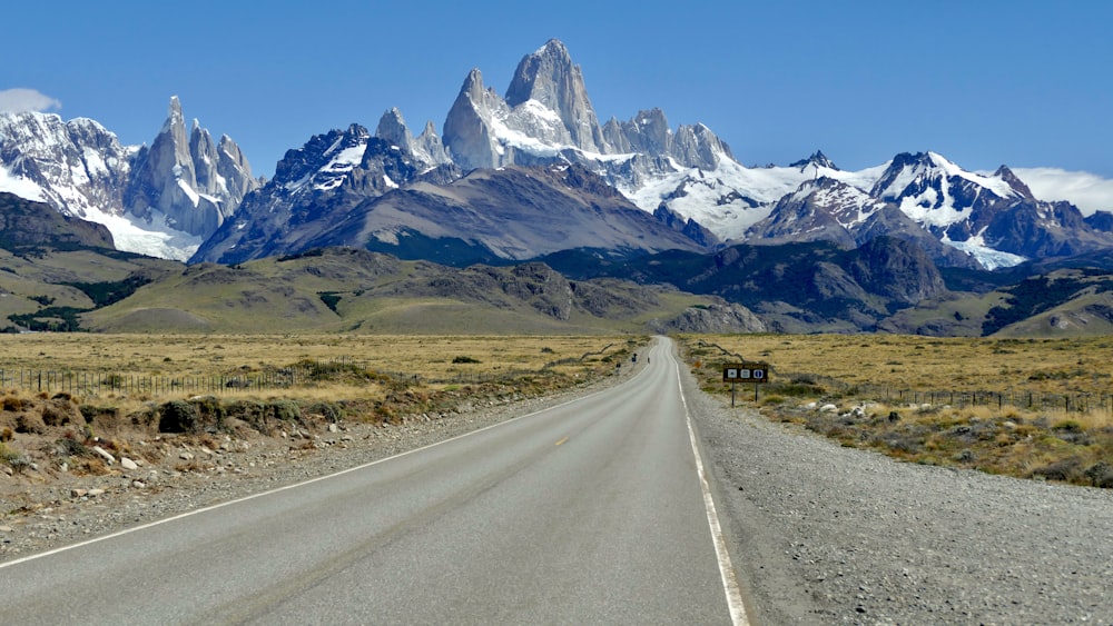 gray asphalt road near mountain range under blue sky during daytime