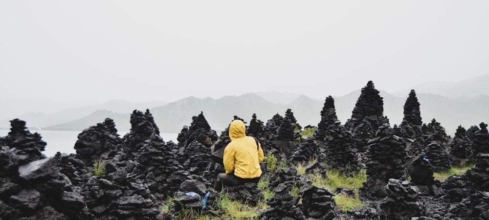 man in yellow hoodie sitting on rock formation during daytime
