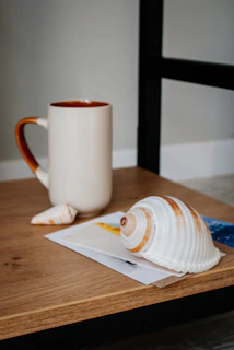 A collection of personalized mugs and hats arranged on a weathered wooden table with seashell accents.