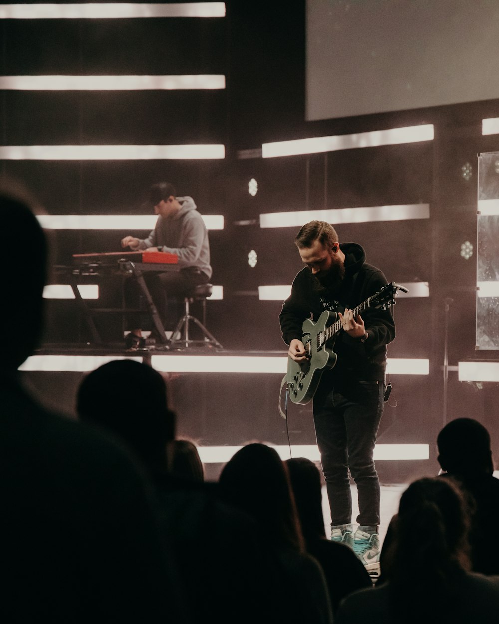 man in black and white long sleeve shirt playing guitar on stage