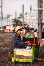 man in black jacket and brown hat sitting on green plastic crate