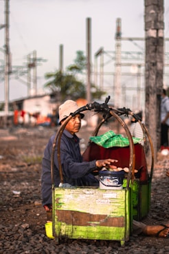 man in black jacket and brown hat sitting on green plastic crate