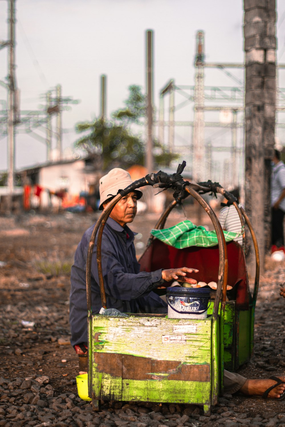 man in black jacket and brown hat sitting on green plastic crate